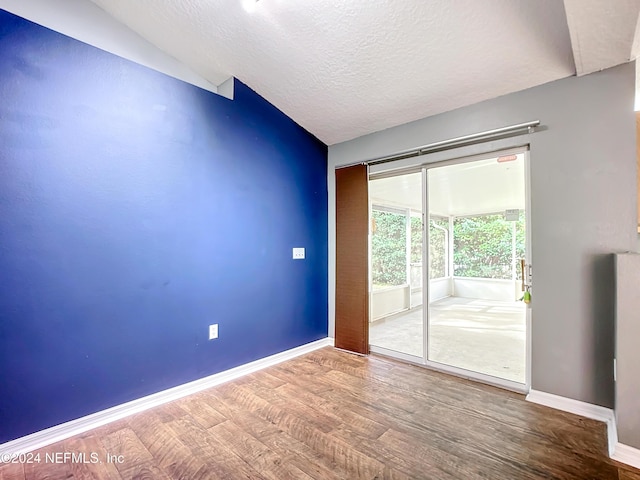 empty room with a textured ceiling, hardwood / wood-style floors, and vaulted ceiling