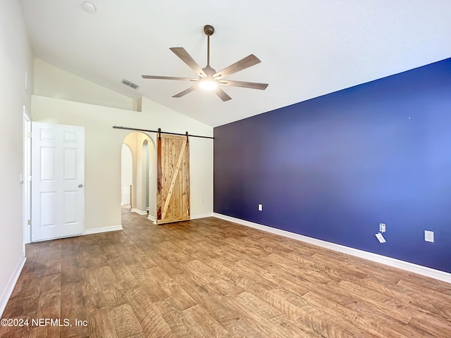 unfurnished room featuring a barn door, ceiling fan, hardwood / wood-style floors, and high vaulted ceiling