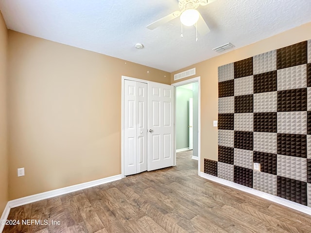 unfurnished bedroom with hardwood / wood-style floors, ceiling fan, a textured ceiling, and a closet