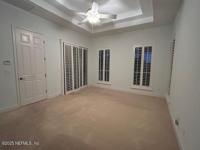 unfurnished bedroom with a tray ceiling, ceiling fan, and carpet flooring