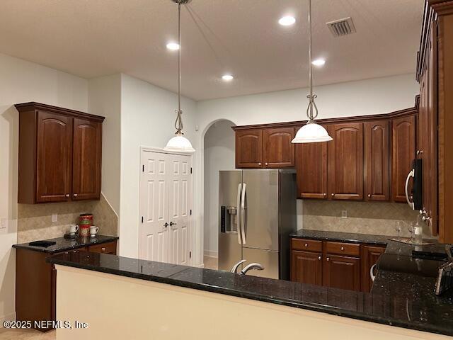 kitchen with stainless steel fridge, hanging light fixtures, and dark stone counters