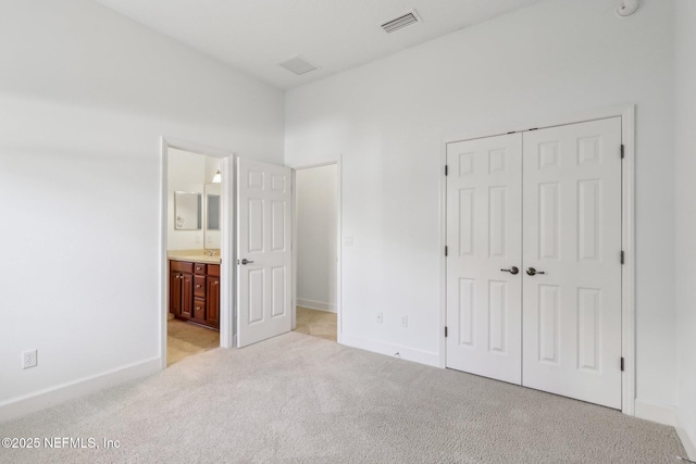 unfurnished bedroom featuring ensuite bathroom, a closet, a towering ceiling, and light colored carpet