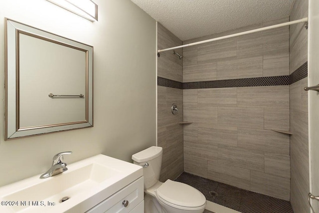 bathroom with a textured ceiling, vanity, toilet, and tiled shower