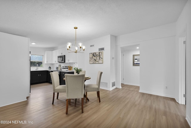 dining space with a textured ceiling, an inviting chandelier, light hardwood / wood-style flooring, and sink