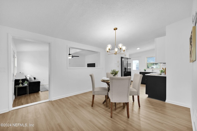 dining area with ceiling fan with notable chandelier, vaulted ceiling, a textured ceiling, and light hardwood / wood-style flooring