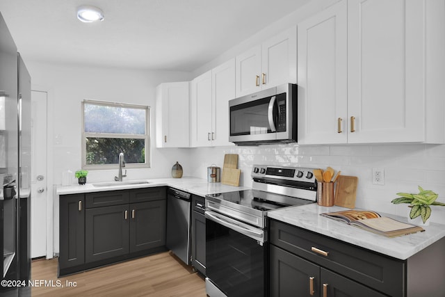 kitchen featuring light stone countertops, white cabinetry, sink, light hardwood / wood-style floors, and appliances with stainless steel finishes