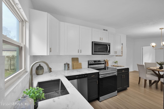 kitchen with white cabinets, decorative light fixtures, appliances with stainless steel finishes, and light hardwood / wood-style flooring