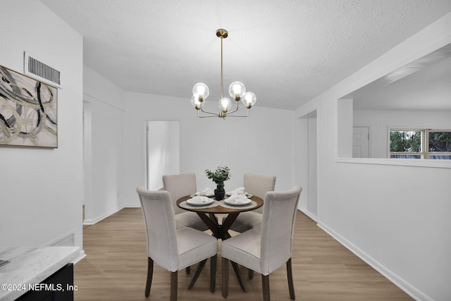 dining room featuring light hardwood / wood-style floors, a textured ceiling, and an inviting chandelier