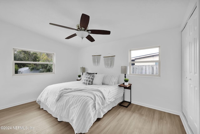 bedroom with ceiling fan, light hardwood / wood-style floors, multiple windows, and a closet