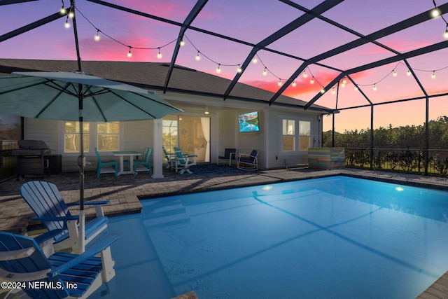 pool at dusk featuring glass enclosure, a patio area, and grilling area