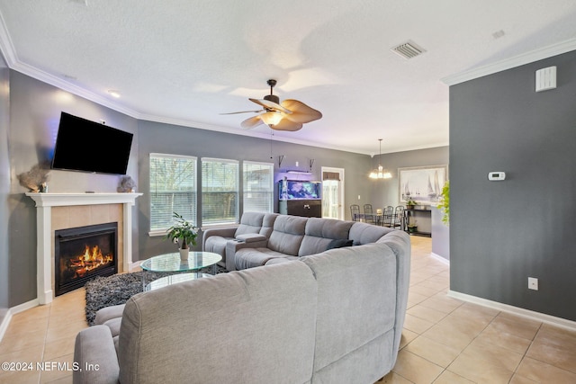 living room featuring ceiling fan with notable chandelier, crown molding, light tile patterned floors, a textured ceiling, and a tiled fireplace