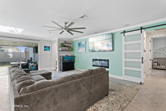 living room with ornamental molding, built in shelves, ceiling fan, light tile patterned floors, and a barn door