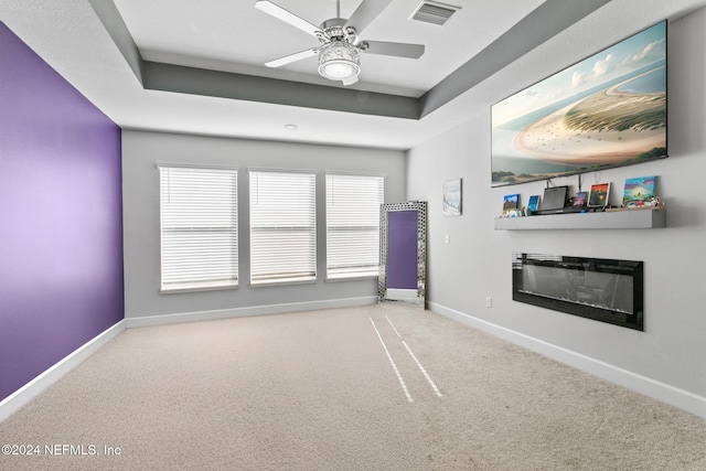 carpeted empty room with ceiling fan and a tray ceiling