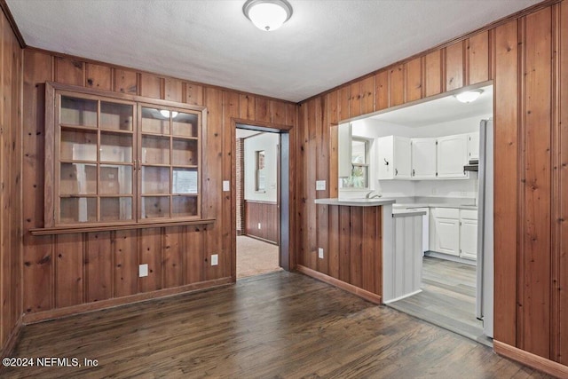 kitchen featuring dark hardwood / wood-style floors, wood walls, white cabinetry, and a textured ceiling