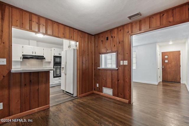 kitchen featuring backsplash, wooden walls, dark wood-type flooring, black appliances, and white cabinetry