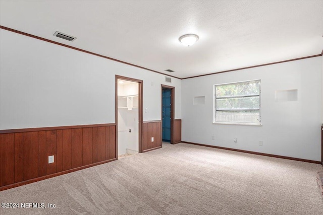 unfurnished bedroom featuring a textured ceiling, light colored carpet, crown molding, and wooden walls