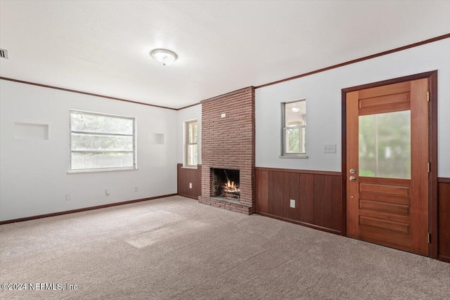 unfurnished living room featuring wood walls, light colored carpet, ornamental molding, and a brick fireplace