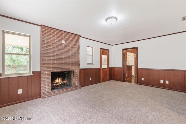 unfurnished living room with carpet flooring, wood walls, crown molding, and a fireplace