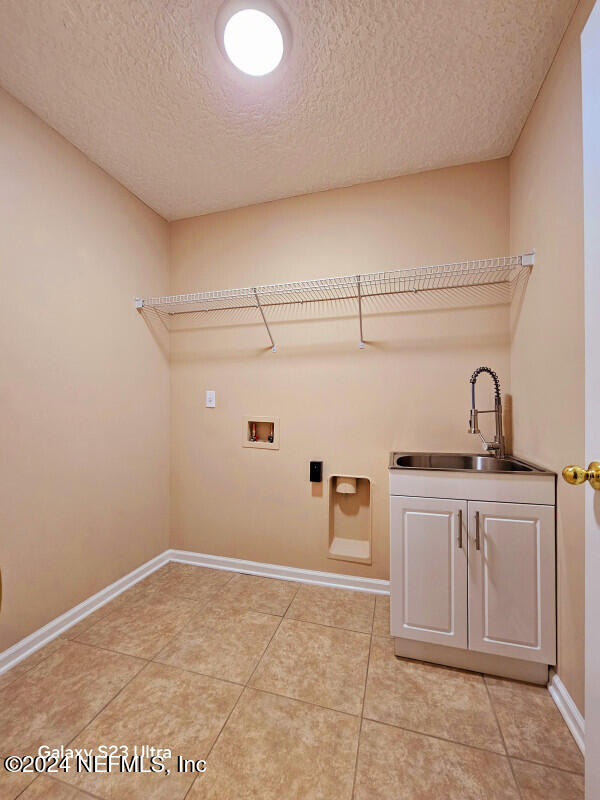 clothes washing area featuring cabinets, washer hookup, a textured ceiling, sink, and light tile patterned flooring