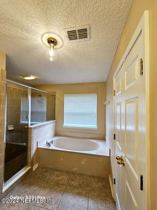 bathroom with tile patterned flooring, shower with separate bathtub, and a textured ceiling