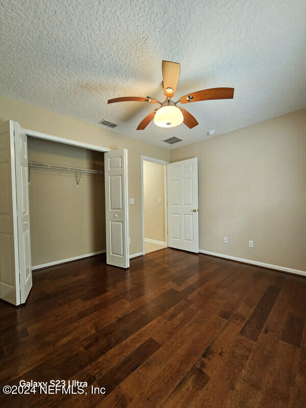 unfurnished bedroom featuring a closet, ceiling fan, dark hardwood / wood-style flooring, and a textured ceiling