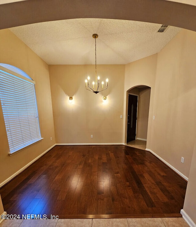 unfurnished dining area featuring hardwood / wood-style flooring, a textured ceiling, and a chandelier