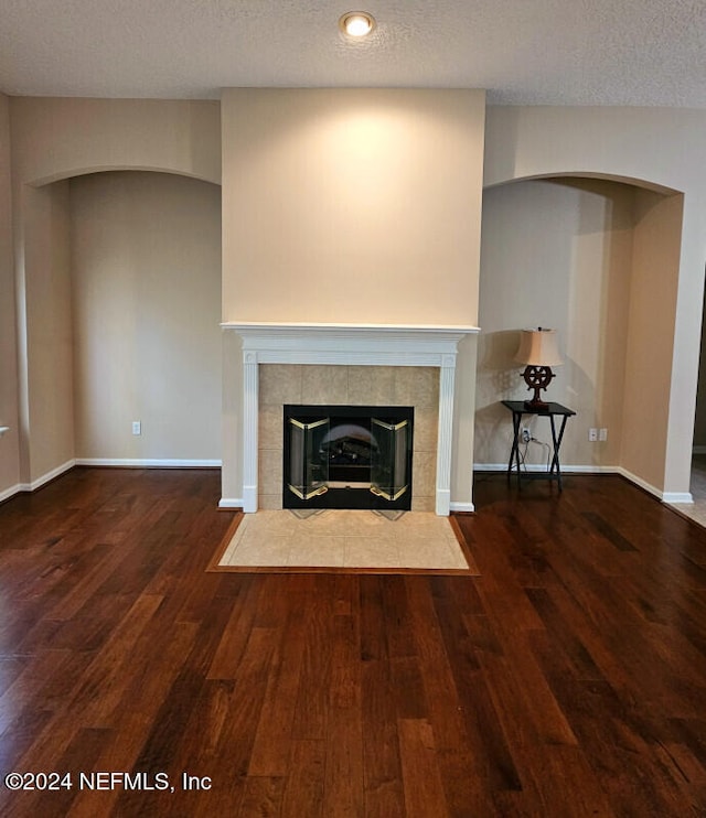 unfurnished living room with a textured ceiling, dark wood-type flooring, and a tiled fireplace