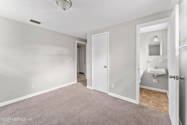 unfurnished bedroom featuring carpet, ensuite bathroom, a closet, and sink