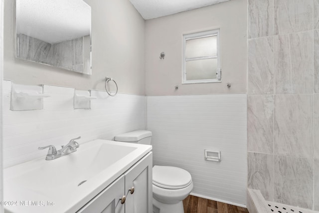 bathroom featuring walk in shower, vanity, wood-type flooring, tile walls, and toilet