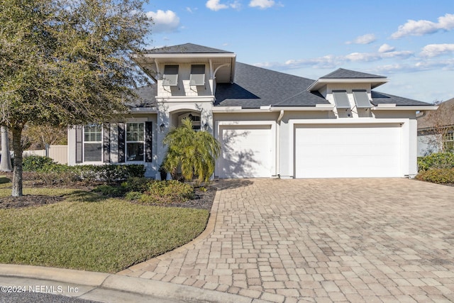 view of front of house with a front yard, roof with shingles, stucco siding, a garage, and decorative driveway