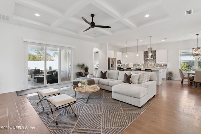 living room featuring beam ceiling, ceiling fan with notable chandelier, hardwood / wood-style flooring, and coffered ceiling