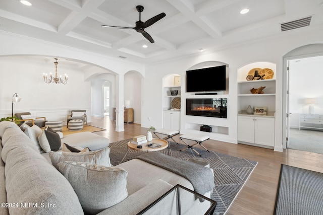 living room featuring light wood-type flooring, coffered ceiling, built in shelves, ceiling fan with notable chandelier, and beam ceiling