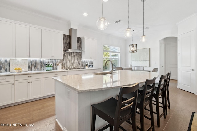 kitchen featuring a center island with sink, white cabinets, sink, light hardwood / wood-style flooring, and wall chimney exhaust hood