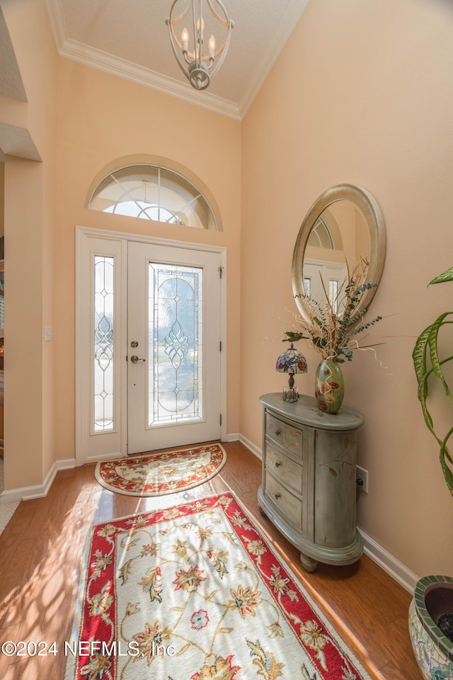 entryway with wood-type flooring, crown molding, high vaulted ceiling, and an inviting chandelier