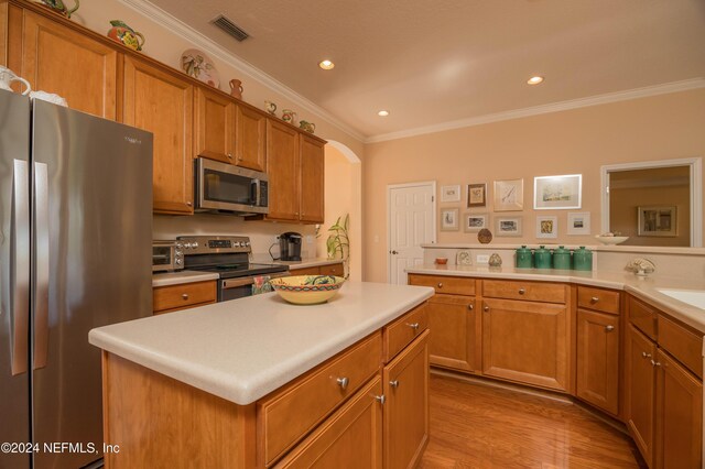 kitchen with sink, a kitchen island, ornamental molding, light hardwood / wood-style floors, and stainless steel appliances