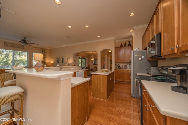 kitchen with stainless steel appliances, crown molding, light hardwood / wood-style floors, a breakfast bar, and a kitchen island