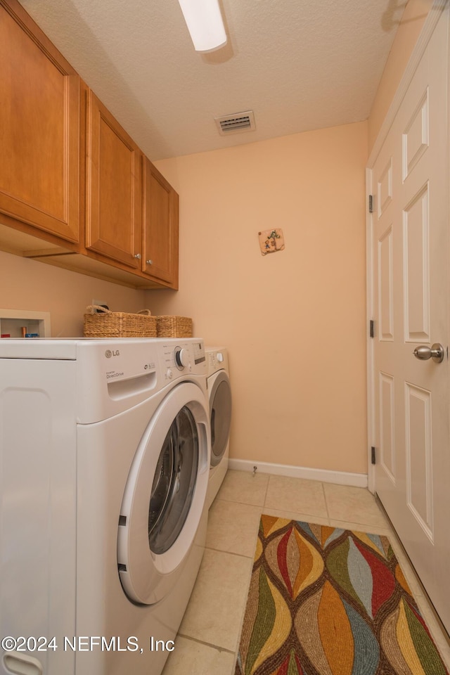 laundry area featuring washing machine and clothes dryer, light tile patterned floors, cabinets, and a textured ceiling