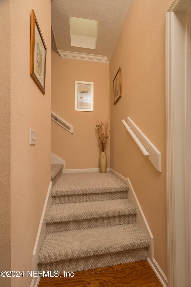 stairway featuring a textured ceiling and crown molding