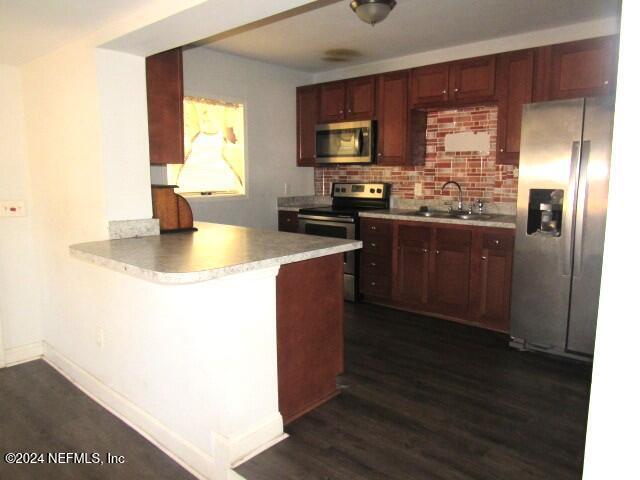 kitchen featuring kitchen peninsula, appliances with stainless steel finishes, dark wood-type flooring, and sink