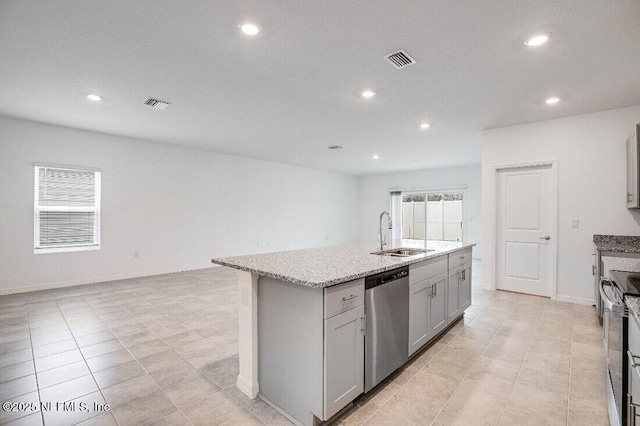 kitchen with appliances with stainless steel finishes, an island with sink, sink, gray cabinetry, and light stone countertops