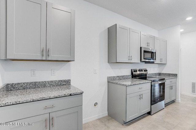 kitchen featuring stainless steel appliances, light tile patterned flooring, light stone countertops, and gray cabinetry