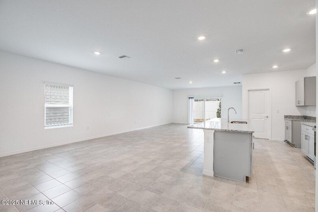 kitchen with sink, a breakfast bar area, a kitchen island with sink, gray cabinetry, and light stone countertops