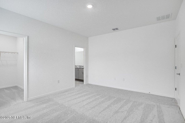 unfurnished bedroom with ensuite bathroom, a spacious closet, light carpet, a textured ceiling, and a closet