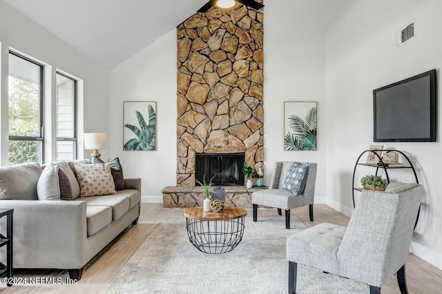 living room featuring high vaulted ceiling, light hardwood / wood-style floors, and a stone fireplace