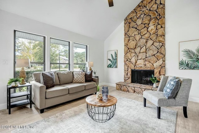 living room featuring high vaulted ceiling, light hardwood / wood-style floors, a stone fireplace, and a wealth of natural light