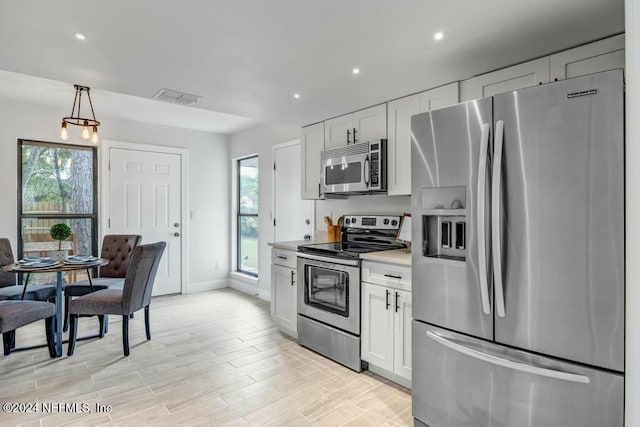 kitchen featuring hanging light fixtures, stainless steel appliances, white cabinetry, and plenty of natural light