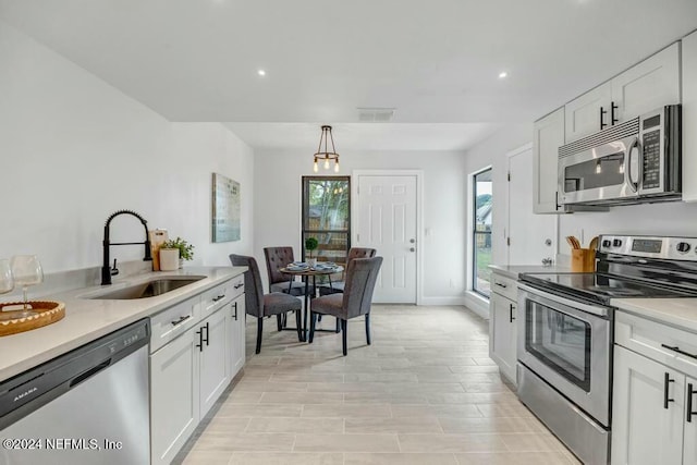 kitchen featuring white cabinets, appliances with stainless steel finishes, hanging light fixtures, and sink