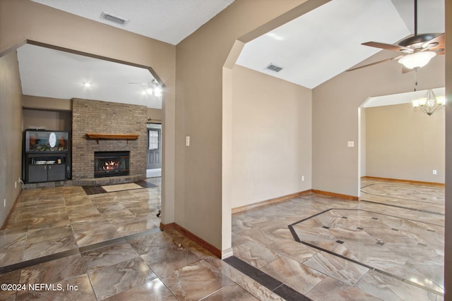 unfurnished living room featuring ceiling fan with notable chandelier, a textured ceiling, a stone fireplace, and lofted ceiling