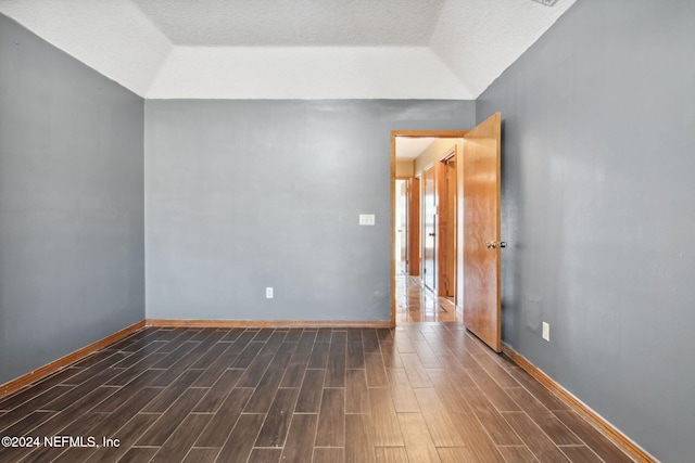 empty room featuring vaulted ceiling, dark hardwood / wood-style flooring, and a textured ceiling