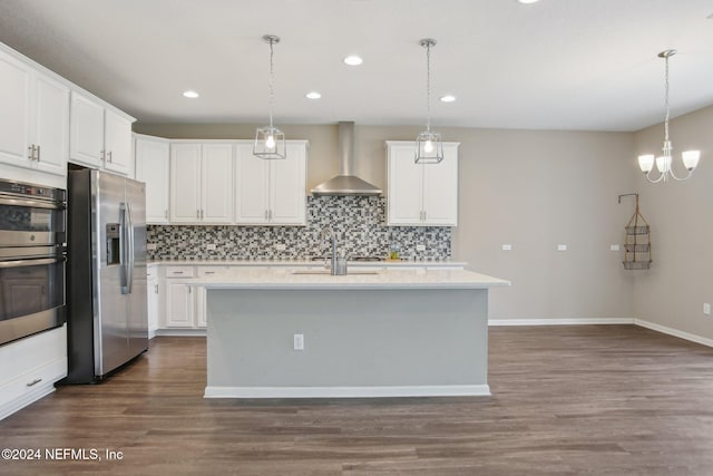 kitchen with wall chimney range hood, stainless steel appliances, white cabinetry, and a center island with sink